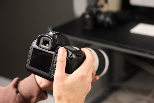 Photographer with professional camera at desk indoors, closeup