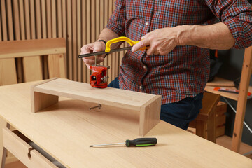 Relaxing hobby. Senior man with hacksaw and vise assembling wooden shelf in workshop, closeup