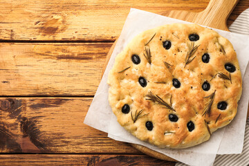 Delicious focaccia bread with olives and rosemary on wooden table, top view. Space for text