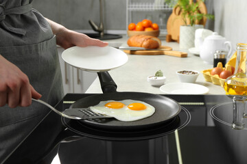 Woman taking fried eggs from frying pan in kitchen, closeup