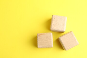 Wooden cubes on yellow background, flat lay. Space for text