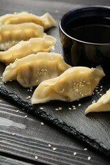 Tasty boiled gyoza (dumplings) with soy sauce and sesame on black wooden table, closeup