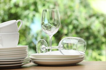 Different clean dishware, cups and glasses on wooden table against blurred green background
