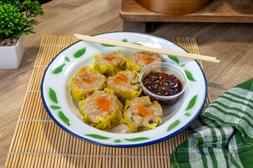 A traditional Chinese food. A plate of dim sum on a white tin plate with chili oil and chopsticks.