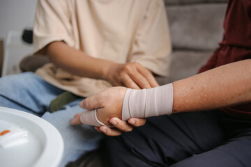 Obraz premium Son Wrapping His Grandfather Wrist And Arm With Bandage Around Injured Hand At Home