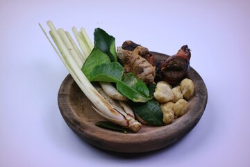 Various kinds of fresh herbs and spices are arranged on a wooden plate, consisting of lemongrass stalks, galangal, lime leaves, ginger, candlenuts. isolated on a white background.