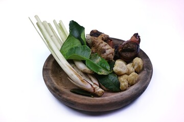 Various kinds of fresh herbs and spices are arranged on a wooden plate, consisting of lemongrass stalks, galangal, lime leaves, ginger, candlenuts. isolated on a white background.