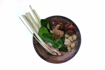 Various kinds of fresh herbs and spices are arranged on a wooden plate, consisting of lemongrass stalks, galangal, lime leaves, ginger, candlenuts. isolated on a white background.