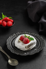 pavlova meringue dessert with raspberries and cream on a black background