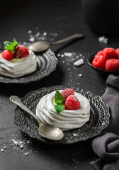 pavlova meringue dessert with raspberries and cream on a black background