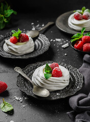 pavlova meringue dessert with raspberries and cream on a black background