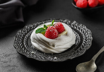 pavlova meringue dessert with raspberries and cream on a black background