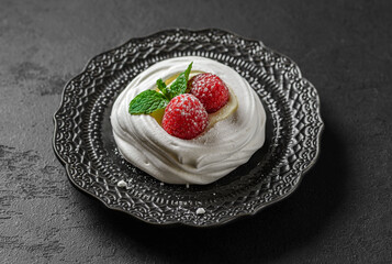 pavlova meringue dessert with raspberries and cream on a black background