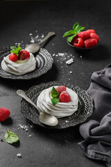 pavlova meringue dessert with raspberries and cream on a black background