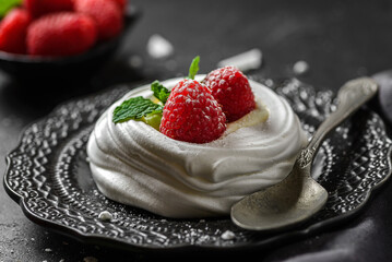 pavlova meringue dessert with raspberries and cream on a black background
