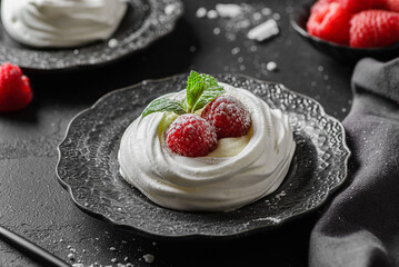 pavlova meringue dessert with raspberries and cream on a black background