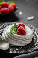 pavlova meringue dessert with raspberries and cream on a black background