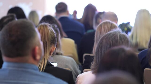 Crowd of people are sitting in a room, some of them are wearing ties. Scene is one of formality and professionalism