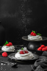 pavlova meringue dessert with raspberries and cream on a black background