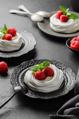pavlova meringue dessert with raspberries and cream on a black background