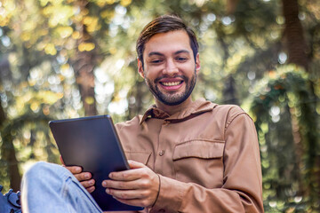 Fototapeta premium Smiling man using tablet in park, enjoying digital nomad lifestyle