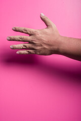 Outstretched human hand with fingers extended in a reaching gesture, captured against a pink background, symbolizing connection, help, or request in a clear, expressive and minimal layout.