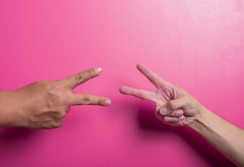 Two Asian hands both making a peace sign, set against a pink background, symbolizing unity, friendship, or a playful moment. The V-shape fingers convey positivity, victory, or nonverbal communication.
