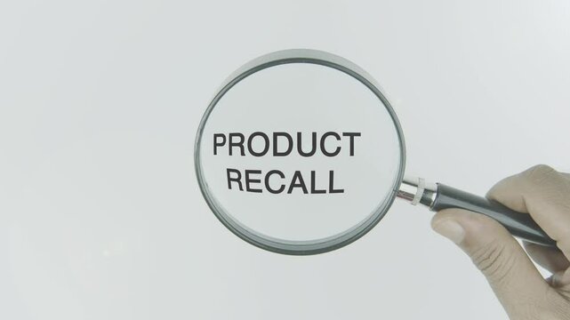 Product recall text or word highlighted by a magnifying glass in a hand on a white background, symbolizing focus on the action of retrieving faulty or unsafe products from the market for safety