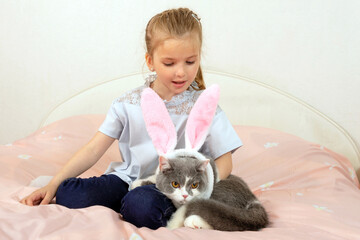beautiful little happy girl is playing with cute rabbit-eared cat on bed at home
