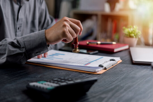 Financial approval and business agreement concept featuring a hand holding a seal stamp on a document. Ideal for management, accounting, and contracts.
