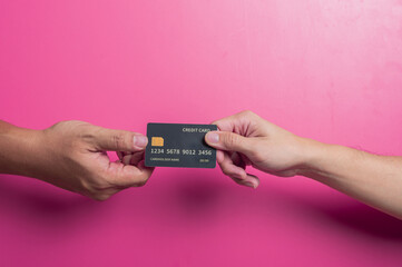 Close-up of an Asian hand holding a sleek black credit card with chip and contactless icon over a pink background, illustrating luxury, finance, and modern digital payment in studio lighting.