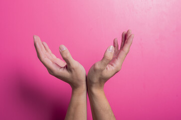 Two Asian hands held upward and cupped together in a symmetrical, open gesture against a pink background, symbolizing offering, prayer, gratitude, or receiving in a calm and peaceful composition.