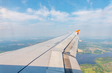 View of airplane wing, blue skies and green land during landing. Airplane window view.