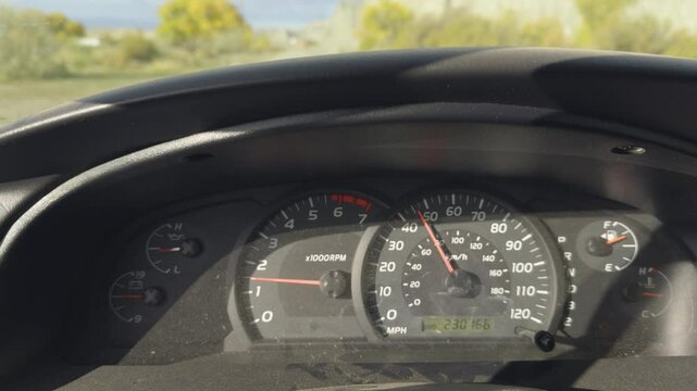 Close-up of a vehicle dashboard showing the speedometer, tachometer, and fuel gauge while driving on a sunny day