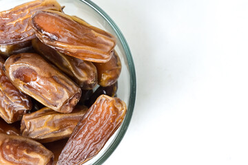Top view of kurma tunisia or sweet dried dates palm fruits in a little glass bowl. Isolated on white background. clipping path. Close up, Half view. Copy space, empty space, free space.