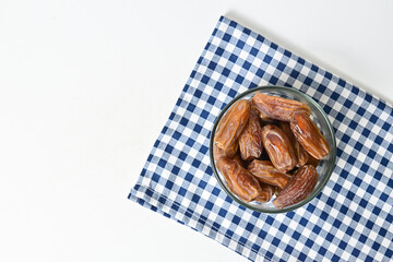 Top view of kurma tunisia or sweet dried dates palm fruits in a little glass bowl with napkin on below. Isolated on white background. clipping path. Flat lay. Empty space, copy space, free space.