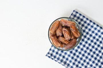 Top view of kurma tunisia or sweet dried dates palm fruits in a little glass bowl with napkin on below. Isolated on white background. clipping path. Flat lay. Empty space, copy space, free space.