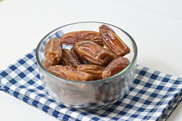 Close up view of kurma tunisia or sweet dried dates palm fruits in a little glass bowl isolated on napkin background. 