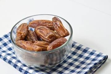 Close up view of kurma tunisia or sweet dried dates palm fruits in a little glass bowl isolated on napkin background. Copy space, empty space, free space.