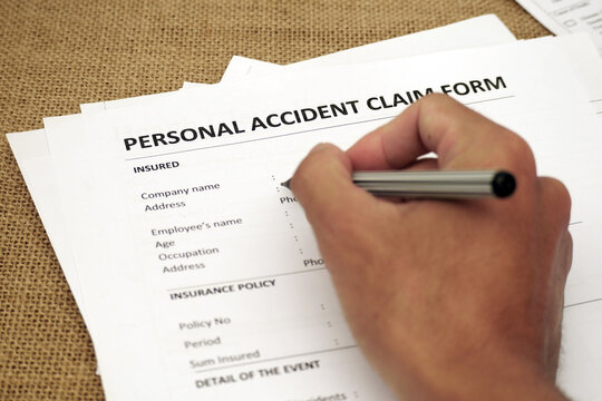A hand filling out a personal accident claim form, symbolizing documentation, insurance processing, and financial protection after an incident
