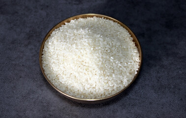 Raw rice in a brass bowl is placed in a dark background.  Healthy ingredient rice.
