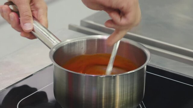 Chef stiring fruit mash with a spoon in stainless steel pot on electric stove panel