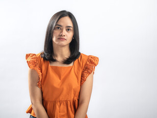Unhappy Southeast Asian woman with straight black hair in orange ruffled blouse and jeans, standing...