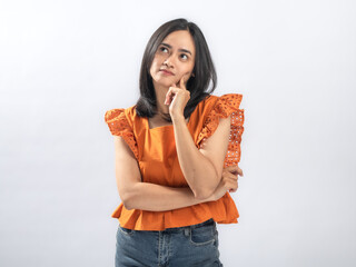 Pensive Southeast Asian woman with straight black hair in orange ruffled blouse and jeans standing...