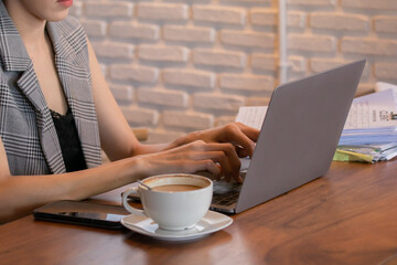 Young professional businesswoman working intently on her laptop at a wooden table in cafe, surrounded by paperwork and coffee cup, a business owner female focused on stock market trading and analyzing