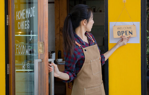 Business startup entrepreneur Asian female happy smiling change the close sign to open sign ready to welcome customers, coffee shop owner or staff worker lifestyles working concept