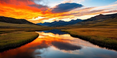 Fototapeta premium A stunning sunset reflects on a tranquil river, surrounded by mountains and golden fields, creating a picturesque landscape.