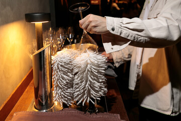The hands of a male bartender use a commercial drying machine to polish a wine glass in close-up