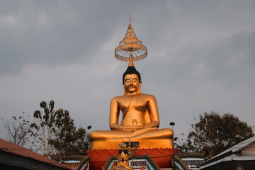Obraz premium Majestic Golden Buddha Statue Situated Beneath a Dramatic Cloudy Sky Displaying Beauty