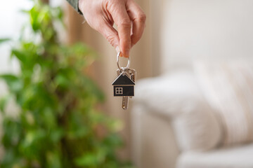 Hand holding keys with house shaped keychain in front of blurred background, representing new home purchase, rental agreement, or mortgage approval
